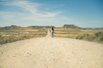 Rear view of woman walking on dirt road in desert