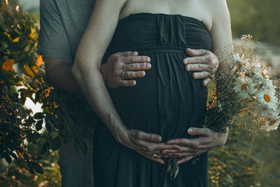 Pregnant woman and her husband hugging her tummy standing outdoors surrounded by nature. pregnancy,