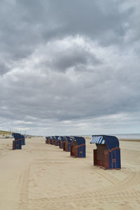 Hooded beach chairs on shore against sky