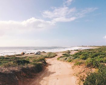 Scenic view of path in beach against cloudy sky