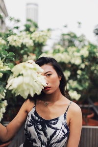 Portrait of young woman standing by flowering plants