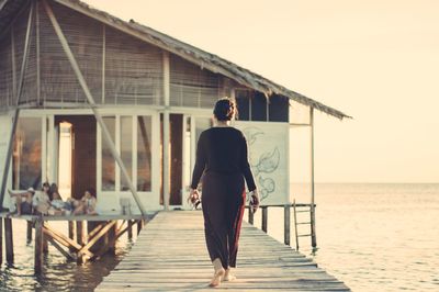 Rear view of man walking on pier over sea against sky