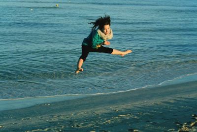 Portrait of excited woman jumping with legs apart at beach