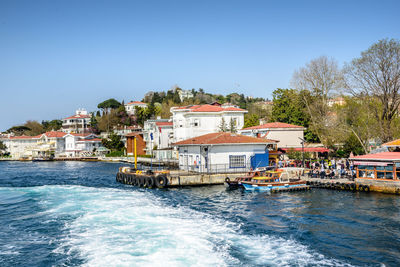 Buildings by sea against clear blue sky