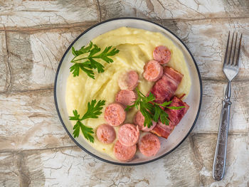 Breakfast with mashed potatoes, fried bacon and sausages, parsley sprigs on a light plate, top view