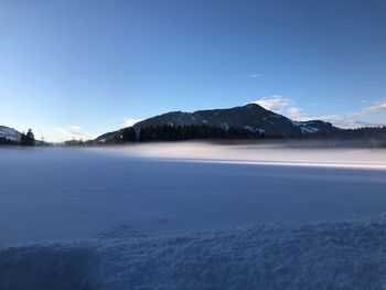 Scenic view of lake and snowcapped mountains against blue sky