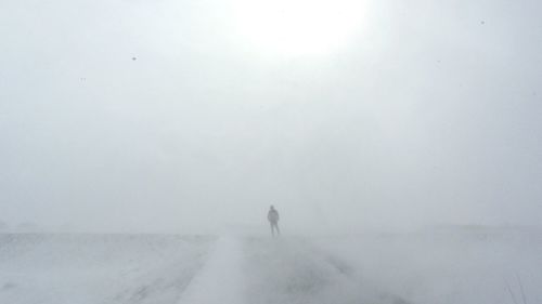 Man walking on snow covered landscape in foggy weather