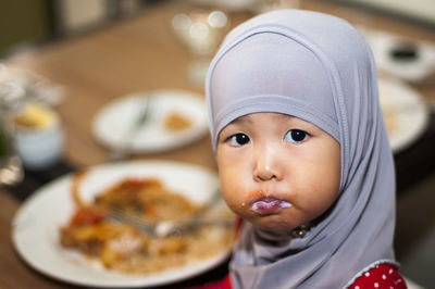 Portrait of girl wearing hijab while mouth filled with food at restaurant