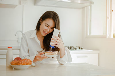 Young woman using phone while sitting on table at home