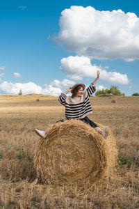 Woman standing on hay bales on field against sky