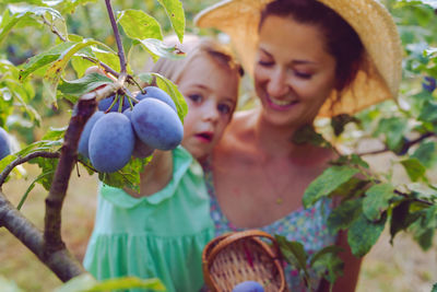 Mother and daughter by fruits growing on tree