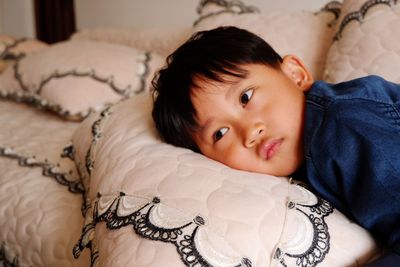 Cute boy looking away while lying on bed at home