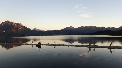 Scenic view of mountain range by lake against sky during sunset