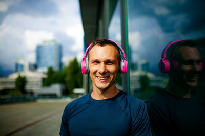 Young sportsman with earphones smiling and looking at camera in city.