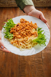 A plate of bolognese decorated with herbs in women's hands. vertical photo