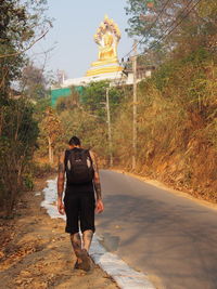 Traveler walking on road by plants against buddha temple