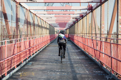 Back view of anonymous cyclist with helmet riding bike among red metal bridge structure in new york city