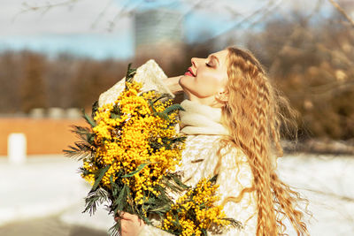 Portrait of a young woman with blond hair holding a bouquet of mimosa in her hands. spring.