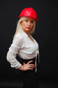 Portrait of businesswoman wearing red hardhat while posing against black background