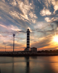 Sea by buildings against sky during sunset