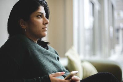 Thoughtful businesswoman holding smart phone while sitting at office lobby