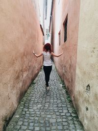 Full length rear view of woman walking on cobblestone