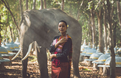 Portrait of smiling woman standing with elephant in forest