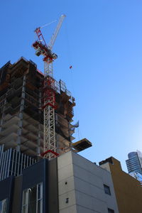Low angle view of crane by building against clear sky