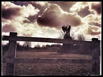 Fence on field against cloudy sky