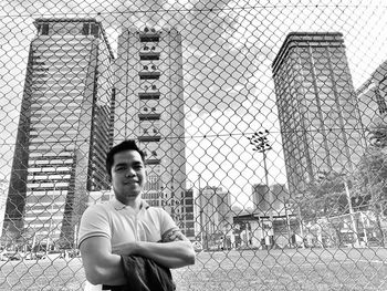 Portrait of young man standing by chainlink fence