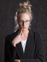 Portrait of young woman holding eyeglasses against black background