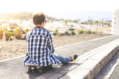 Rear view of boy sitting on skateboard