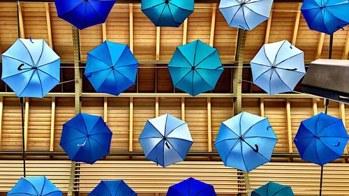 Low angle view of multi colored umbrellas hanging against blue sky