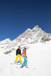 People walking on snowcapped mountain against clear blue sky