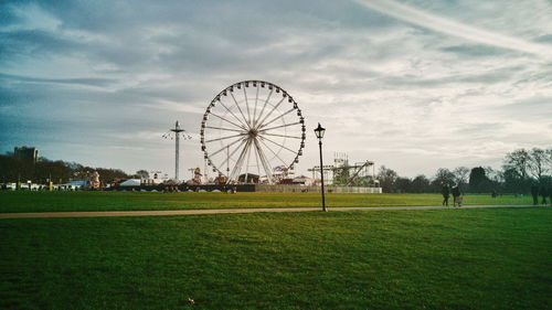 Ferris wheel on field against cloudy sky