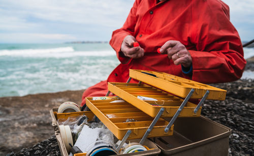 Midsection of man sitting by toolbox at beach