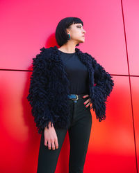 Woman looking away while standing against red wall