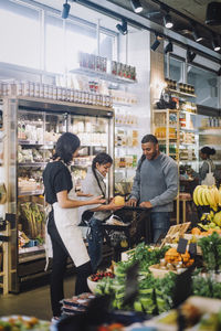 Female sales clerk talking with customers buying groceries at delicatessen