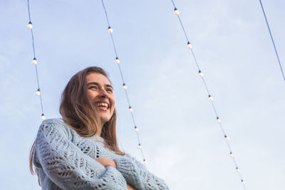 Low angle view of smiling woman looking away while standing against sky