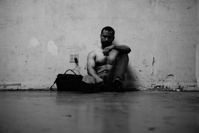Shirtless man sitting by electric plug against wall at home