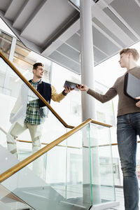 Low angle view of man giving book to friend