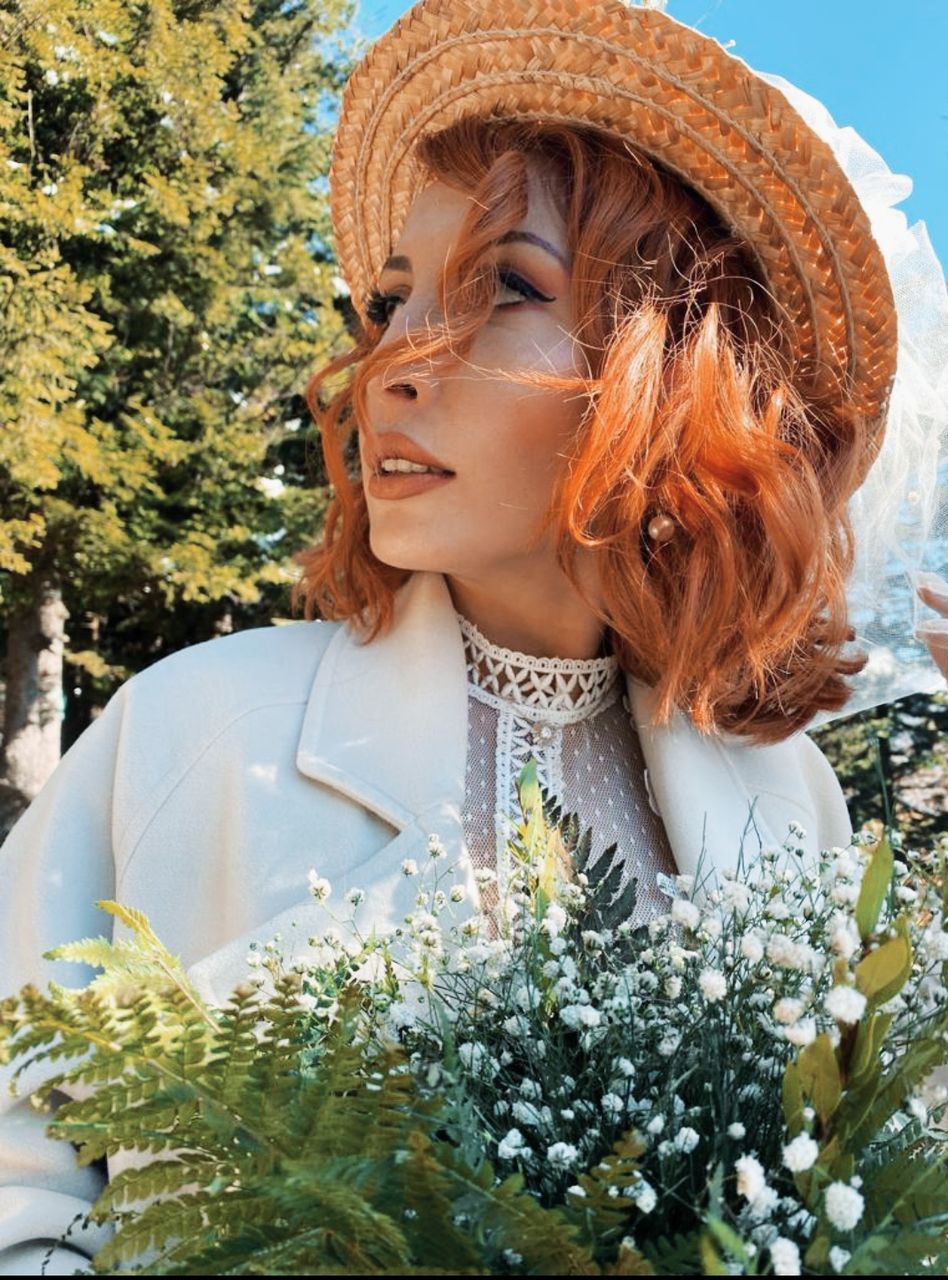 plant, one person, women, adult, nature, flower, young adult, spring, portrait, clothing, lifestyles, leisure activity, flowering plant, headshot, hat, looking, day, smiling, beauty in nature, female, hairstyle, redhead, happiness, outdoors, front view, looking away, growth, standing, tree, person, sunlight, waist up, emotion, casual clothing, fashion, art, long hair, bride, human face, fashion accessory