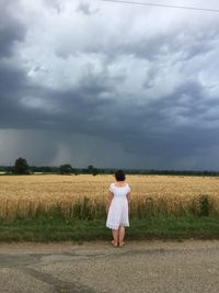 Rear view of woman standing against agricultural field against cloudy sky