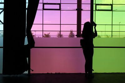 Rear view of silhouette woman standing against glass window