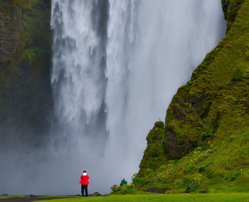 Rear view of person standing against majestic waterfall