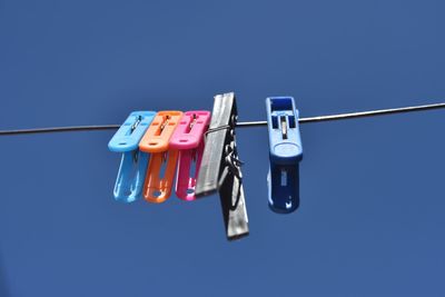 Low angle view of clothespins on clothesline against blue sky