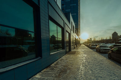 Cars on city street against sky during sunset