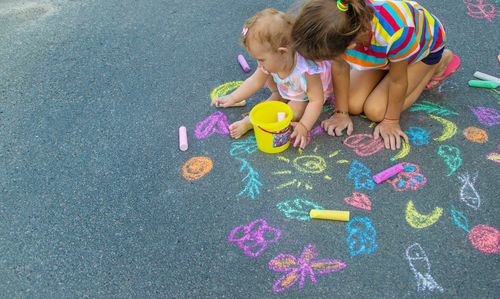 Girl with sister playing with chalk on sidewalk