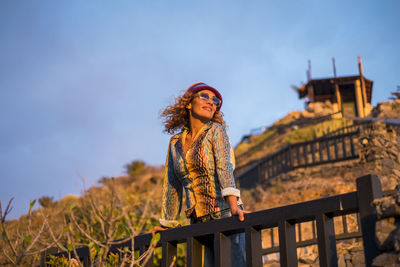 Low angle view of smiling mature woman standing by railing against sky