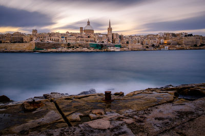 View of buildings by sea against cloudy sky